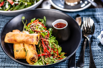 A plate of three spring rolls, green salad and chilli sauce