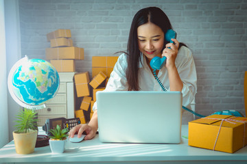 Young Women use the phone to contact the customer business owner working at home office with packaging on background. online shopping SME entrepreneur or freelance working concept.