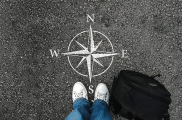  a man with a shoes and backpack is standing next to compass sign on road asphalt