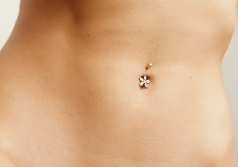 Young woman navel with jewelry - piercing on the umbilicus. - obrazy, fototapety, plakaty