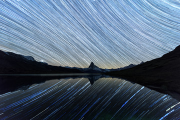 Incredible night view of Stellisee lake with Matterhorn Cervino peak in Swiss Alps. Stars trails moving in blue sky. Zermatt resort location, Switzerland. Landscape astrophotography © Ivan Kmit