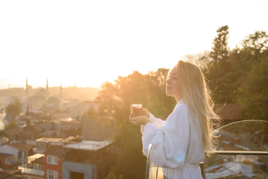 A girl in a bathrobe with a cup of Turkish tea at sunrise on the terrace of a house in Istanbul