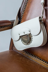 white female clutch on a brown chair, womens bag, clutch hanging on the back of the chair