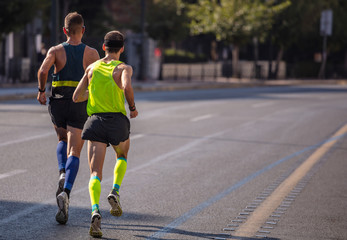Marathon running race, two men runners on city roads, detail on legs,