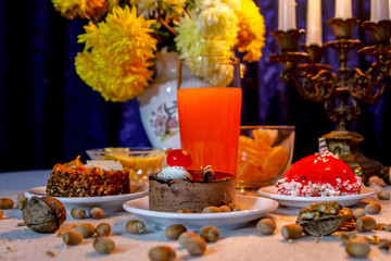 Beautiful evening composition with cakes and candle light.Old candle holder, flowers, cakes, oranges, limon, red orange juice, walnuts and hazelnuts.