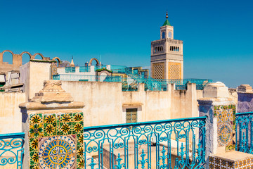 A Tunisian rooftop overlooking Tunis with a bright blue/aqua sky, decorated tiles in the foreground and Tunisian landmark in the background.