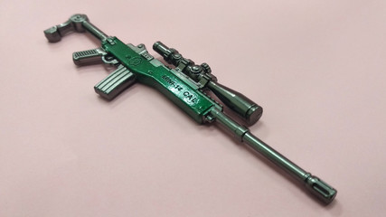A miniature model of military sniper automatic gun in small-scale isolated on red background. Sale as a collector item for military gear collector and hobbyist. 