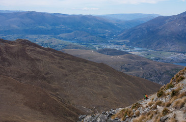 A view from Ben Lomond at a landscape with a person sitting on a rock near Queenstown in New Zealand