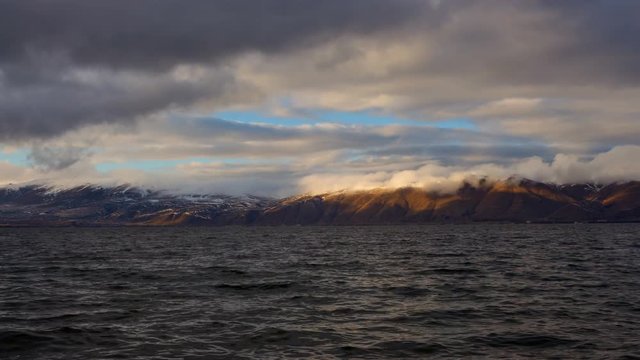 Daytime Timelapse of moving clouds over lake Sevan on background hills. The camera moves away.
