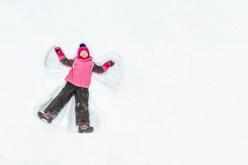 Cute little kid girl in warm ski sport suit making snow angel outdoors. Kid having fun lying on...