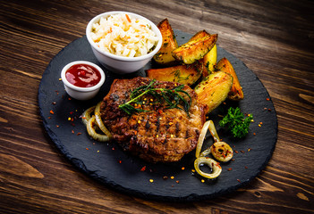 Grilled steak with baked potatoes and vegetables served on black stone plate on wooden table