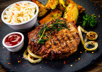 Grilled steak with baked potatoes and vegetables served on black stone plate on wooden table