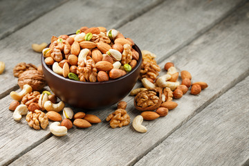 Wooden bowl with mixed nuts on a wooden gray background. Walnut, pistachios, almonds, hazelnuts and cashews, walnut.