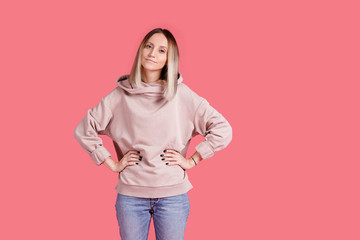 Delicate positive young blond woman in casual clothes with hands on waist on bright pink background. Place for text