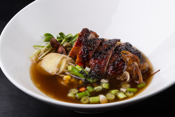 Asian duck noodle soup served with leek and herbs in a white bowl