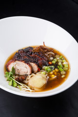Asian duck noodle soup served with leek and herbs in a white bowl