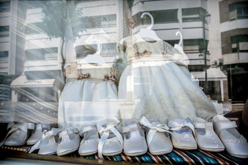 Dresses and shoes to make first communion reflected in showcase, conceptual image