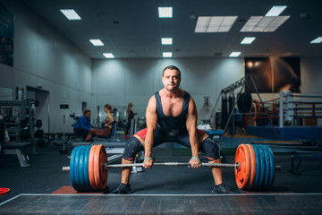 Male weightlifter prepares to pull heavy barbell - obrazy, fototapety, plakaty