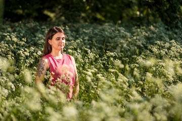 positive young woman meditating in park surrounded by flowers