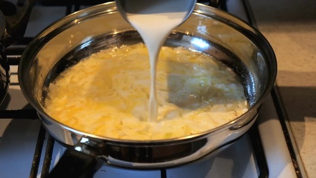 A woman is cooking cream sauce in a pan.