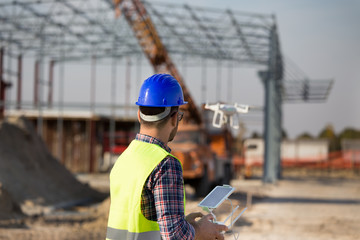Construction worker with drone at building site - obrazy, fototapety, plakaty