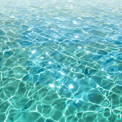 Fototapeta na wymiar Blue transparent water surface with bright sun glare and sunny shining reflections on bottom. Top view of turquoise ripple texture with sunlight refracting through liquid layer.