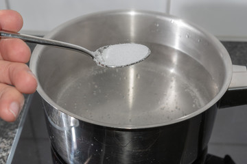 Salz auf dem Löffel in das kochende Wasser schütten