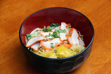 egg noodle and pork wonton with red roasted pork in the Japanese bowl on the wooden table.