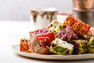 Variety of traditional turkish dessert Turkish Delight different taste and colors rose petals and pistachio nuts on ceramic plate with coffee jezve and milk jug on white marble table. Close up
