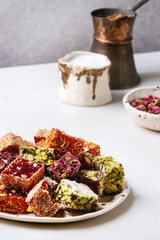 Variety of traditional turkish dessert Turkish Delight different taste and colors rose petals and pistachio nuts on ceramic plate with coffee jezve and milk jug on white marble table