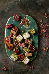 Obraz na płótnie Canvas Variety of traditional turkish dessert Turkish Delight different taste and colors with rose petals and pistachio nuts on turquoise ceramic tray over old dark metal background. Flat lay, space