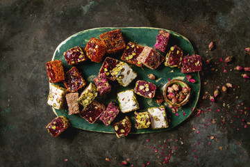 Fototapeta na wymiar Variety of traditional turkish dessert Turkish Delight different taste and colors with rose petals and pistachio nuts on turquoise ceramic tray over old dark metal background. Flat lay, space