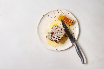 Organic honey in honeycombs with knife in spotted ceramic plate on white marble background. Flat lay, copy space