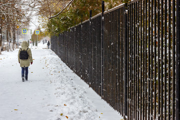 The young person walking on the sidewalk in the cold snowy winter weather