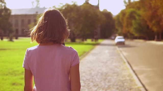 back view student walking on the street turn to the camera with happy smile. beautiful girl with blond hair
