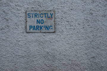Fading dark blue " Strictly no parking " sign on highly textured grey stucco wall