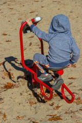 Fototapeta na wymiar toddler boy playing on tractor in the sand on playground