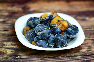 Healthy food concept. Frozen organic plums without stones on a white plate and a rustic wooden table.  