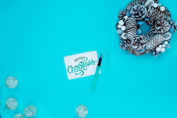 Winter and Christmas wreath with snow , pine cones, and merry christmas hand painted green watercolor lettering isolated on blue background. Top view