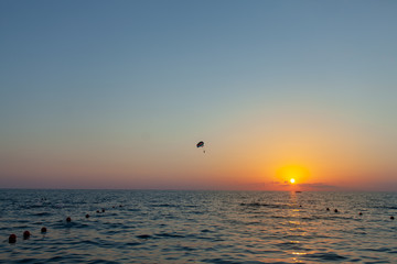 Silhouette of powered paraglider soaring flight over the sea against marvellous orange sunset sky. Paragliding - recreational and competitive adventure sport.