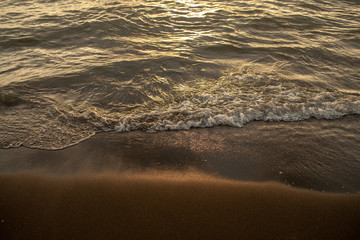 Close up beach wave at sunset. Sun reflecting on serene beach. Soft focus
