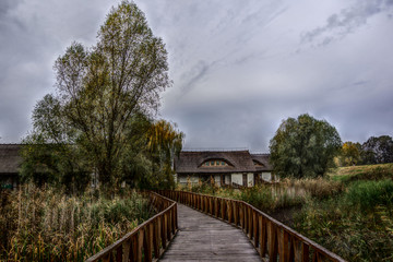 Fototapeta na wymiar Landscape view of wooden path over marsh,leading to two traditional building in background. Kopački rit Nature Park (Amazon of Europe), Croatia.