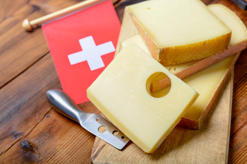Assortment of Swiss cheeses Emmental or Emmentaler medium-hard cheese with round holes, Gruyere, appenzeller and raclette used for traditional cheese fondue and gratin and flag of Switzerland