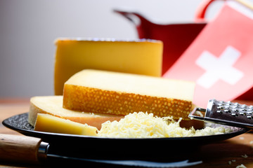 Assortment of Swiss cheeses Emmental or Emmentaler medium-hard cheese with round holes, Gruyere, appenzeller and raclette used for traditional cheese fondue and gratin and flag of Switzerland