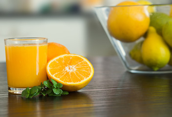 Glass of freshly squeezed orange juice with bowl of fruits on the background.