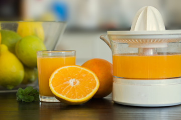 Glass and juicer with freshly squeezed orange juice with bowl of fruits on the background.