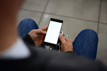 A man holds a cellphone with a white screen in his hands. Looking over male shoulder. The concept of new technologies in everyday life.