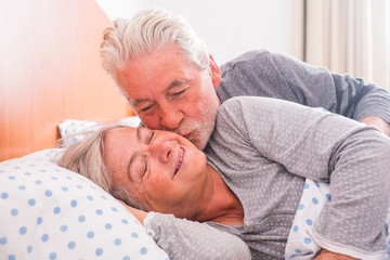 Couple of senior man and woman waking up and smiling with a hug while are in the bed at home. He...