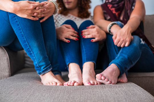 barefoot closeup portrait of three friends at home enjoying friendship sitting on the sofa - casual clothes jeans and fashion concept for modern millennial girls