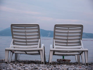 Two empty plastic chaise lounge on sea side at the end of season side view